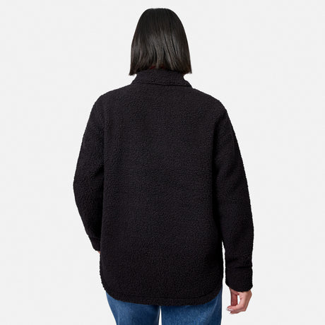 A woman with straight, shoulder-length dark hair is seen from behind, standing against a plain white background, wearing the Free Country Women’s Sherpa Shacket in black and blue jeans.