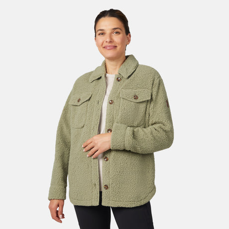 A woman smiles against a white background, wearing the Free Country Women's Sherpa Shacket in light green with an oversized fit, two chest pockets, and black pants.