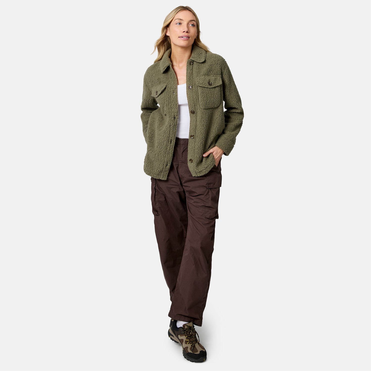 [Model is wearing size S.] A woman modeling an olive green textured button-up jacket over a white top, paired with dark brown cargo pants and camouflage sneakers, against a light gray studio background.