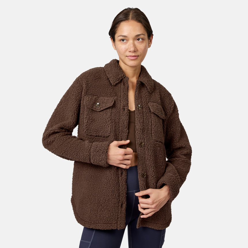 [Model is wearing size S.] A woman modeling a brown sherpa fleece button-up jacket with chest flap pockets, photographed against a clean light gray studio background.