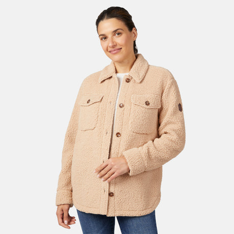 A woman smiles against a white background wearing the Free Country Women's Sherpa Shacket in beige, featuring an oversized fit, front pockets, and super-soft fabric, with one hand resting on the jacket.