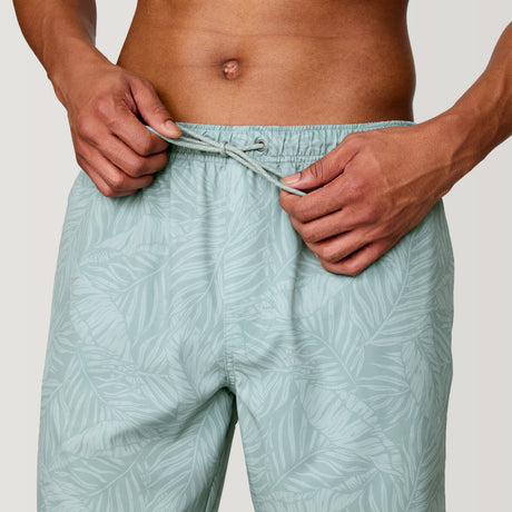 A person adjusts the drawstring on Clearance Men's Palm Heaven Swim Shorts, featuring a light green tone with a subtle palm pattern. Made from recycled polyester—only their torso and hands are visible.