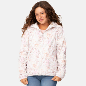 A smiling young person with long, curly brown hair wears the Clearance Girls' Windshear Jacket—wind and water resistant, made from recycled polyester—over a white top and blue jeans, standing against a plain light gray background.