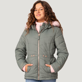 A young girl with wavy brown hair wears a light green Free Country Girls' Bib Puffer Jacket, made from recycled polyester with a hood featuring pink fur trim and water-resistant finish, standing against a plain light gray background.