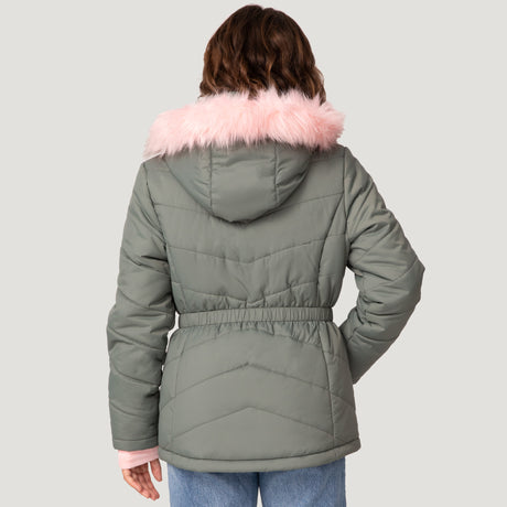 A person is seen from the back, wearing Free Country’s Girls' Bib Puffer Jacket in green recycled polyester with a pink faux fur-lined hood and light pink cuffs, paired with blue jeans, set against a plain light gray background. Water-resistant style meets function.