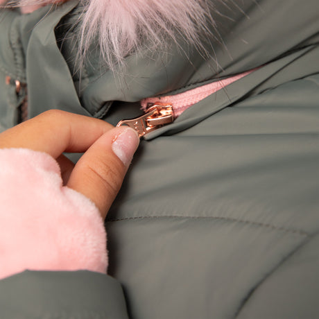 A hand with light pink nail polish zips up the Free Country Girls' Bib Puffer Jacket in sage green, featuring water-resistant recycled polyester, a rose gold zipper, and a fluffy light pink lining and hood trim.