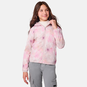 A girl with long brown hair wears the Clearance Girls' Windshear Jacket, a pastel pink and white tie-dye recycled polyester piece, over a white turtleneck and gray cargo pants, standing and smiling against a plain white background.