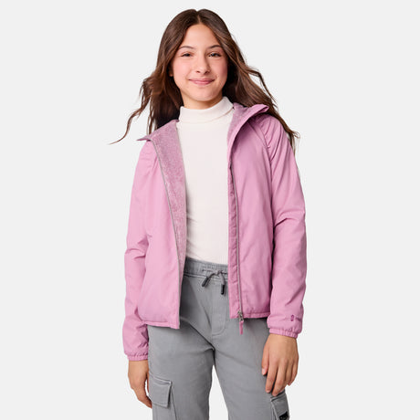 A young girl with long brown hair smiles while wearing the Clearance Girls' Windshear Jacket in light pink over a white turtleneck and gray cargo pants, standing against a plain light background.