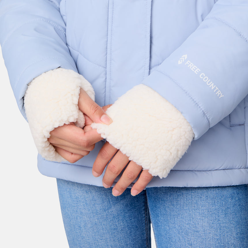 [Samantha is wearing size M] Model wearing a light blue Free Country winter jacket with faux fur-trimmed hood, quilted body, and white fleece-lined cuffs; styled with blue jeans for a casual, cold-weather look.