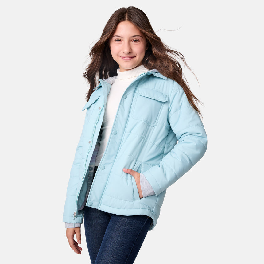 [Samantha is wearing size M.] Model wearing a Free Country light blue quilted jacket with button-front closure, flap chest pockets, and side pockets—layered over a white shirt with dark blue jeans for a casual, cold-weather look.