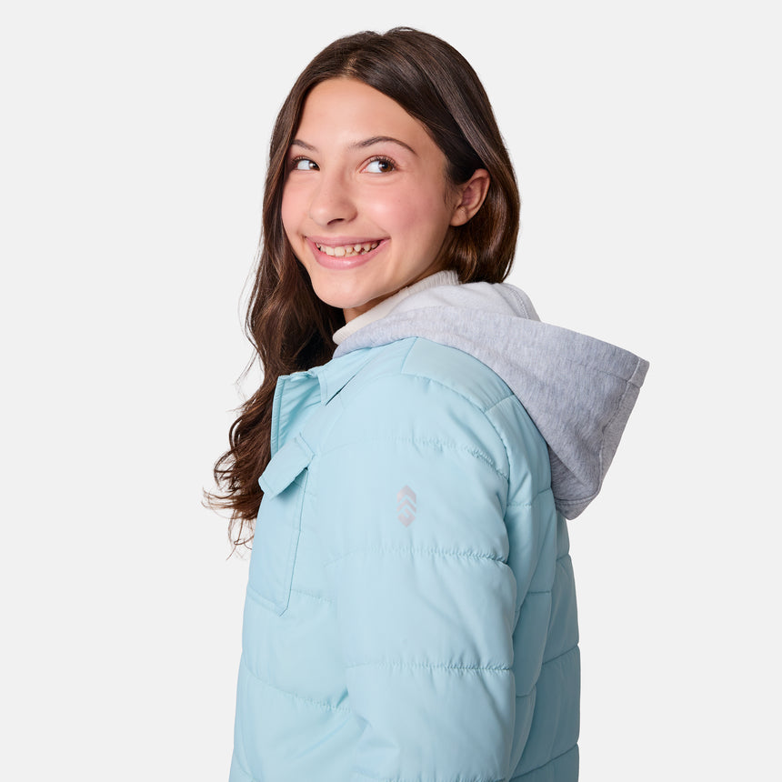 [Samantha is wearing size M.] Model wearing a Free Country light blue quilted jacket with button-front closure, flap chest pockets, and side pockets—layered over a white shirt with dark blue jeans for a casual, cold-weather look.