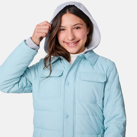 [Samantha is wearing size M.] Model wearing a Free Country light blue quilted jacket with button-front closure, flap chest pockets, and side pockets—layered over a white shirt with dark blue jeans for a casual, cold-weather look.