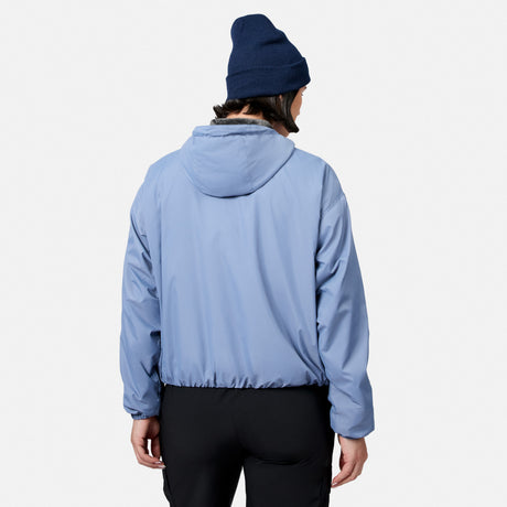 A person models the Women’s Bomber Windshear Jacket by Free Country in light blue, paired with black pants and a dark blue beanie, standing with their back to the camera against a plain white background.