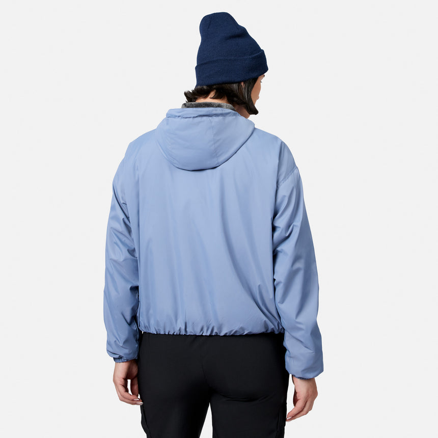 A person models the Women’s Bomber Windshear Jacket by Free Country in light blue, paired with black pants and a dark blue beanie, standing with their back to the camera against a plain white background.