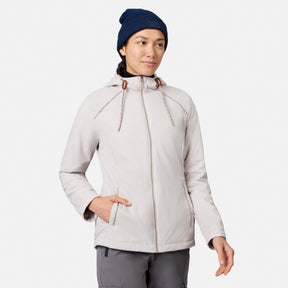 A person wearing a Women’s Anorak Windshear Jacket by Free Country in bisque stands against a white background with one hand in their pocket, looking slightly to the side and smiling softly.