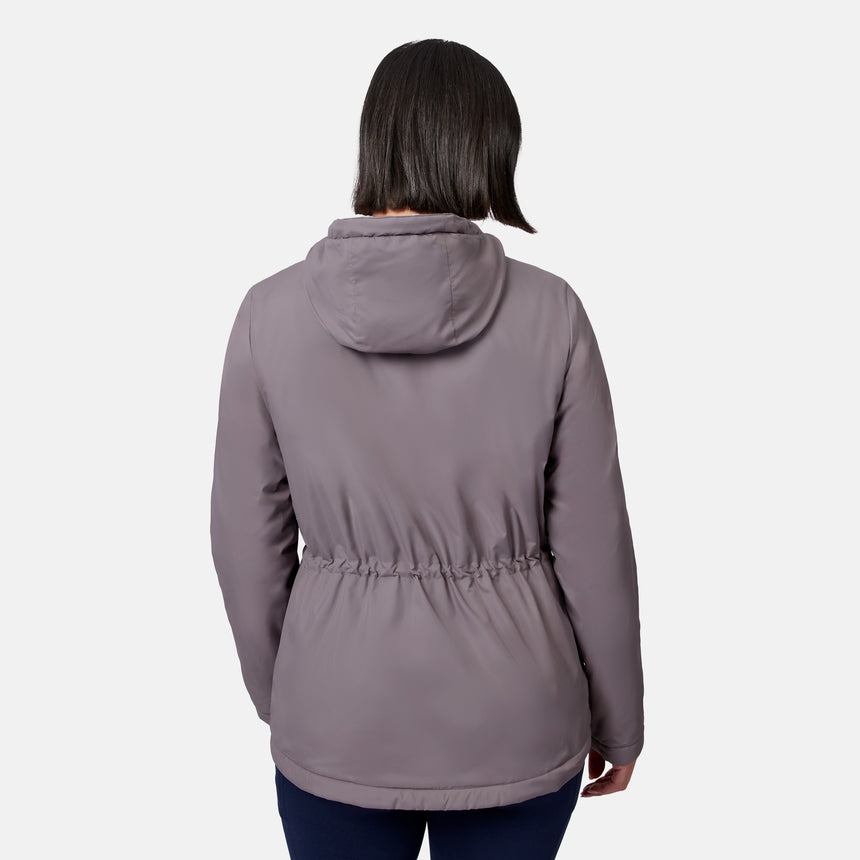 A woman wears the Free Country Women’s Anorak Windshear Jacket in light purple, shown from behind to highlight the drawstring waist and back details, standing against a plain white background.