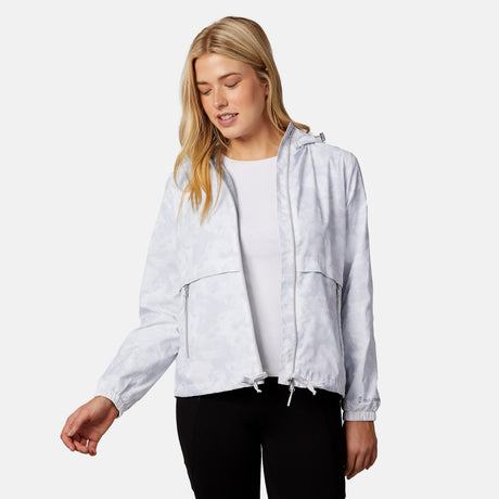 A woman with long blonde hair wears the Clearance Women's Outland Windshear Jacket over a white top and black pants, standing against a plain light background and looking down with a slight smile.