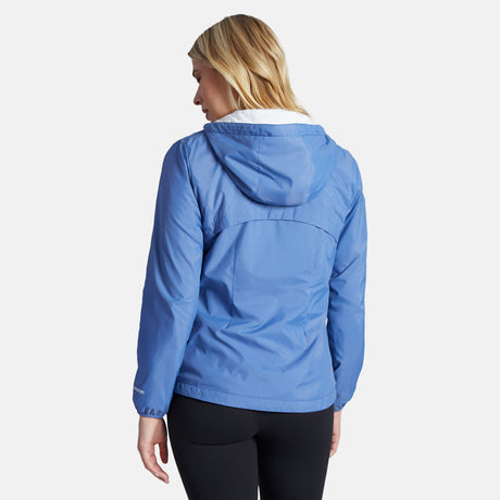 A woman with blonde hair models the Clearance Women's Trek Mate Windshear Jacket in light blue and black pants, facing away from the camera against a plain white background.
