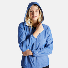 A woman with long blonde hair wears the Clearance Women's Trek Mate Windshear Jacket, zipping it up and holding the hood by her face as she stands calmly against a plain white background.