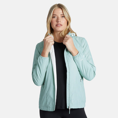 A woman with long blonde hair and a neutral expression stands against a white background, wearing the Clearance Women's Trek Mate Windshear Jacket in light blue over a black top, holding the collar edges with both hands.