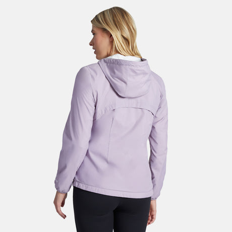 A woman with blonde hair is wearing the Women's Trek Mate Windshear Jacket by Clearance in light purple with black pants, facing away from the camera against a plain white background.