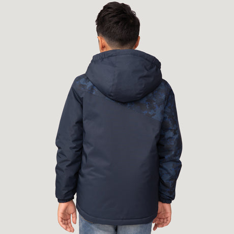 A boy with short, dark hair is seen from behind wearing the Free Country Boys' Multi Rip Stop Boarder Jacket in navy blue with a digital camo sleeve and back design, paired with light blue jeans against a plain light background.