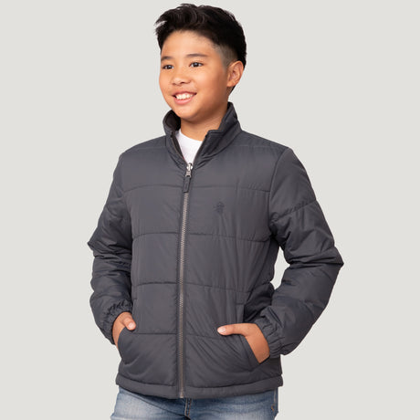 [Model is wearing a size Medium.] Young boy wearing the Free Country Boys' 3-in-1 Systems Jacket in a dark grey with a hood and subtle chest pattern, smiling against a plain background.