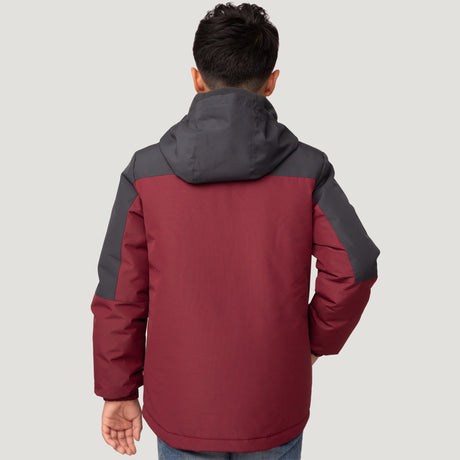[Model is wearing a size Medium.] Young boy wearing the Free Country Boys' 3-in-1 Systems Jacket in a dark red with a hood and subtle chest pattern, smiling against a plain background.