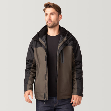 A man with short brown hair and a beard wears the Men's FreeCycle® Jack Frost 3-in-1 Systems Jacket by Clearance, black and olive green, over a black shirt and blue jeans, standing against a plain light gray background.