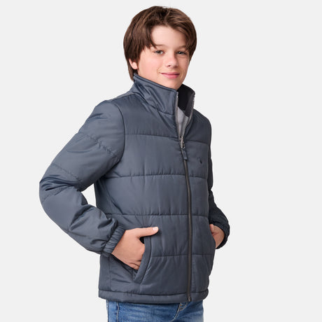 [River is wearing size M.] Young boy wearing the Free Country Boys' 3-in-1 Systems Jacket in a light grey with a hood and subtle chest pattern, smiling against a plain background.