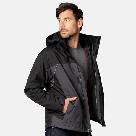 A man wearing a black and gray Men's FreeCycle® Jack Frost 3-in-1 Systems Jacket by Clearance over a gray t-shirt stands with one hand in his pocket, looking to his left against a plain light background.