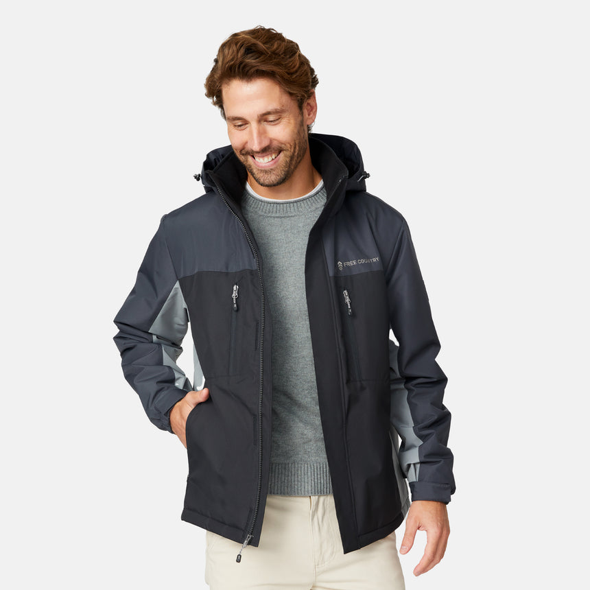 [Matt is 6'2" wearing size M.] Men’s Free Country black zip-front jacket with gray hood, sleeves, and side panels—features dual zippered chest pockets and side pockets for practical, cold-weather functionality. Paired with beige pants for a clean, transitional outdoor look.