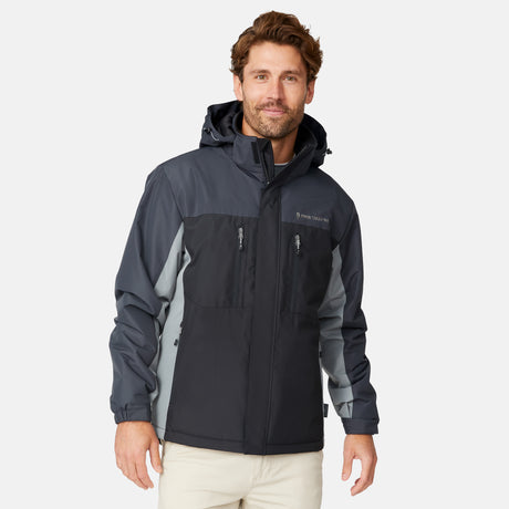 [Matt is 6'2" wearing size M.] Men’s Free Country black zip-front jacket with gray hood, sleeves, and side panels—features dual zippered chest pockets and side pockets for practical, cold-weather functionality. Paired with beige pants for a clean, transitional outdoor look.