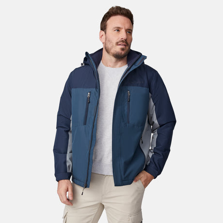 [Joe is 6'0" wearing size M.] Men’s Free Country hooded zip-front jacket in blue with gray paneling—featuring dual vertical zippered chest pockets and side hand pockets. Paired with light khaki pants for a clean, functional look suited to cold-weather layering and outdoor versatility.