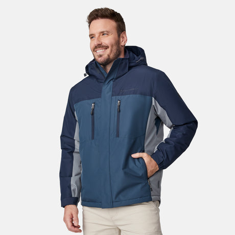 [Joe is 6'0" wearing size M.] Men’s Free Country hooded zip-front jacket in blue with gray paneling—featuring dual vertical zippered chest pockets and side hand pockets. Paired with light khaki pants for a clean, functional look suited to cold-weather layering and outdoor versatility.