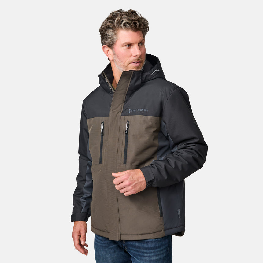 [Kolby is 6'2" wearing size M.]  "Men’s Free Country two-tone zip-front jacket with black upper section and olive green lower panels—features dual vertical zippered chest pockets, side hand pockets, and attached hood. Layered over a green crewneck tee and blue jeans for versatile, outdoor-ready style.