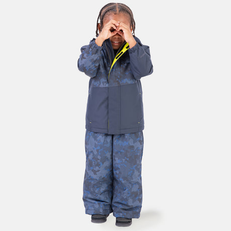 A toddler wears the Free Country Boys' Toddler Boarder Jacket and Bib Pant Set, posing playfully with hands as pretend glasses, dressed in cozy blue patterned outerwear made from recycled polyester.