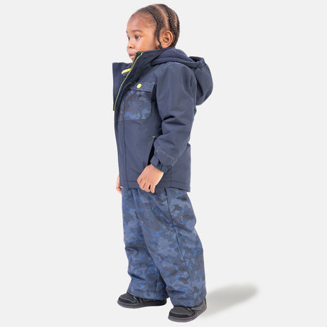 A young child wears the Free Country Boys' Toddler Boarder Jacket and Bib Pant Set, featuring a dark blue water-resistant winter jacket and matching snow pants made from recycled polyester, shown facing left against a white background.