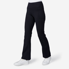 A person in black Women's Trail 2 Town Flare Pants by Free Country, featuring side pockets, is paired with white sneakers and stands against a plain white background.