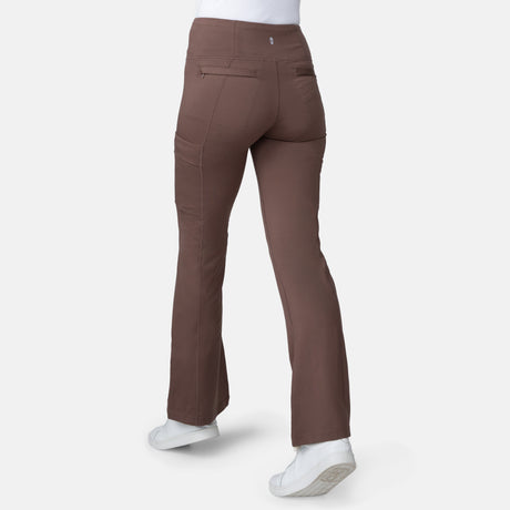A person is shown from the back wearing Free Country Women's Trail 2 Town Flare Pants in brown and white sneakers, standing against a plain white background.