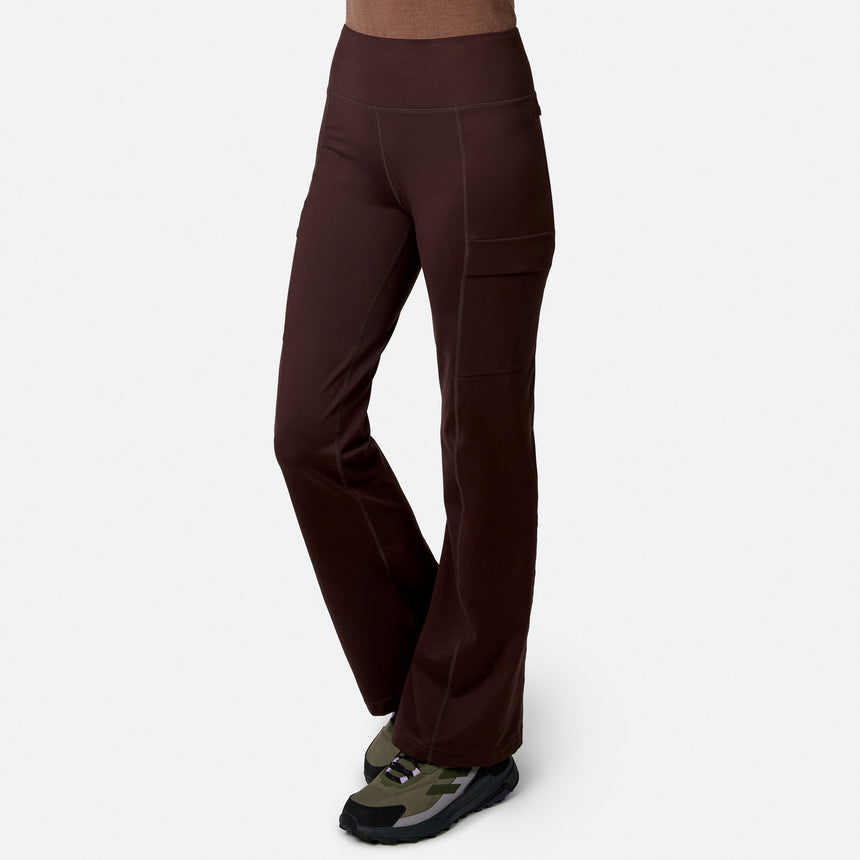Model wears Free Country Women’s Trail 2 Town Flare Pants with visible stitching and side pockets, paired with green and black athletic shoes, against a white background.