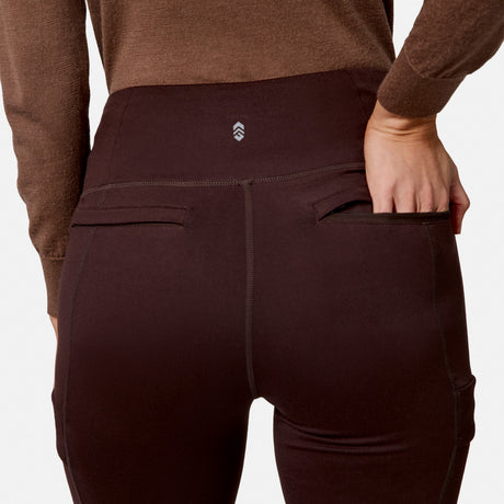 Person wears Free Country Women’s Trail 2 Town Flare Pants in dark brown and a brown top, shown from the back with their right hand partially inside the right back pocket. Background is plain white.