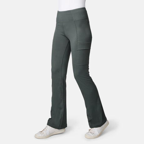 A person wears Free Country Women’s Trail 2 Town Flare Pants in Loden with side pockets and white sneakers, standing against a plain white background.