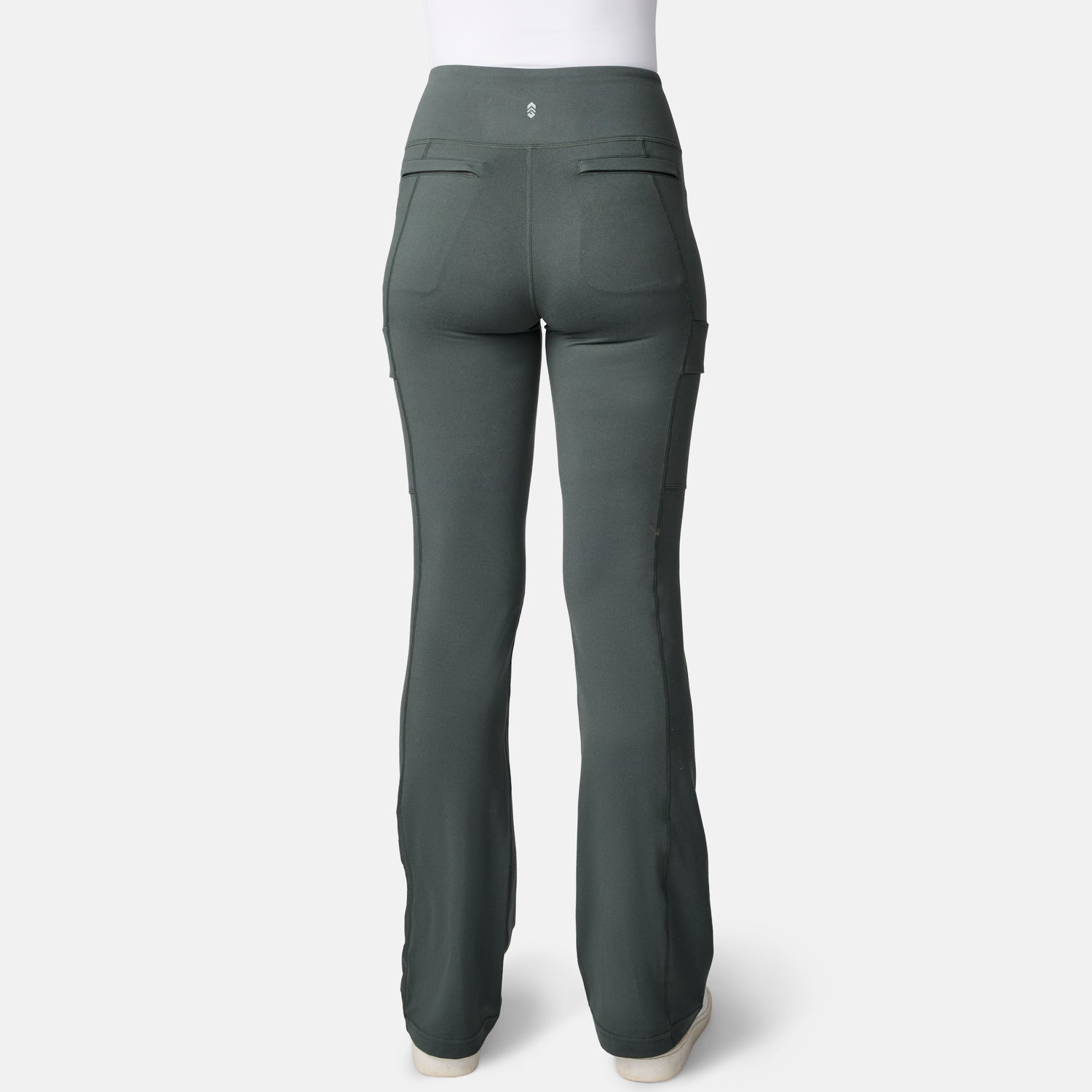 Back view of a person in Free Country Women’s Trail 2 Town Flare Pants—high-waisted, dark green, UPF 50+, two rear pockets, white shoes—shown against a plain white background.