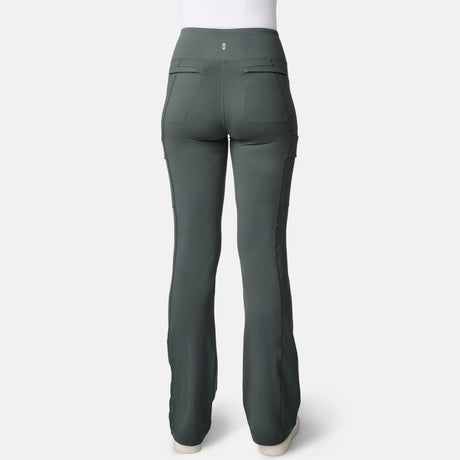 Back view of a person in Free Country Women’s Trail 2 Town Flare Pants—high-waisted, dark green, UPF 50+, two rear pockets, white shoes—shown against a plain white background.