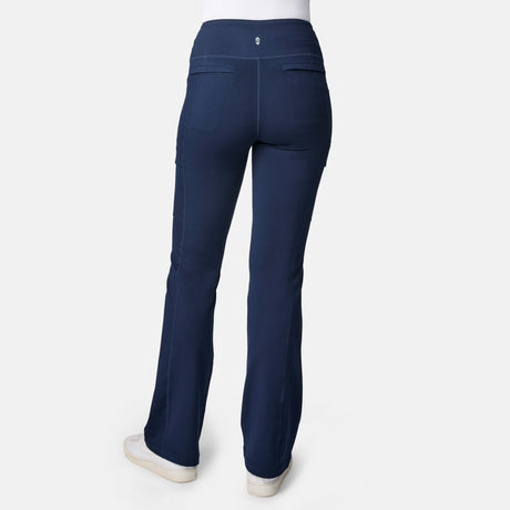 A person wearing navy blue Free Country Women’s Trail 2 Town Flare Pants with UPF 50+ and white sneakers, shown from the back against a plain white background.