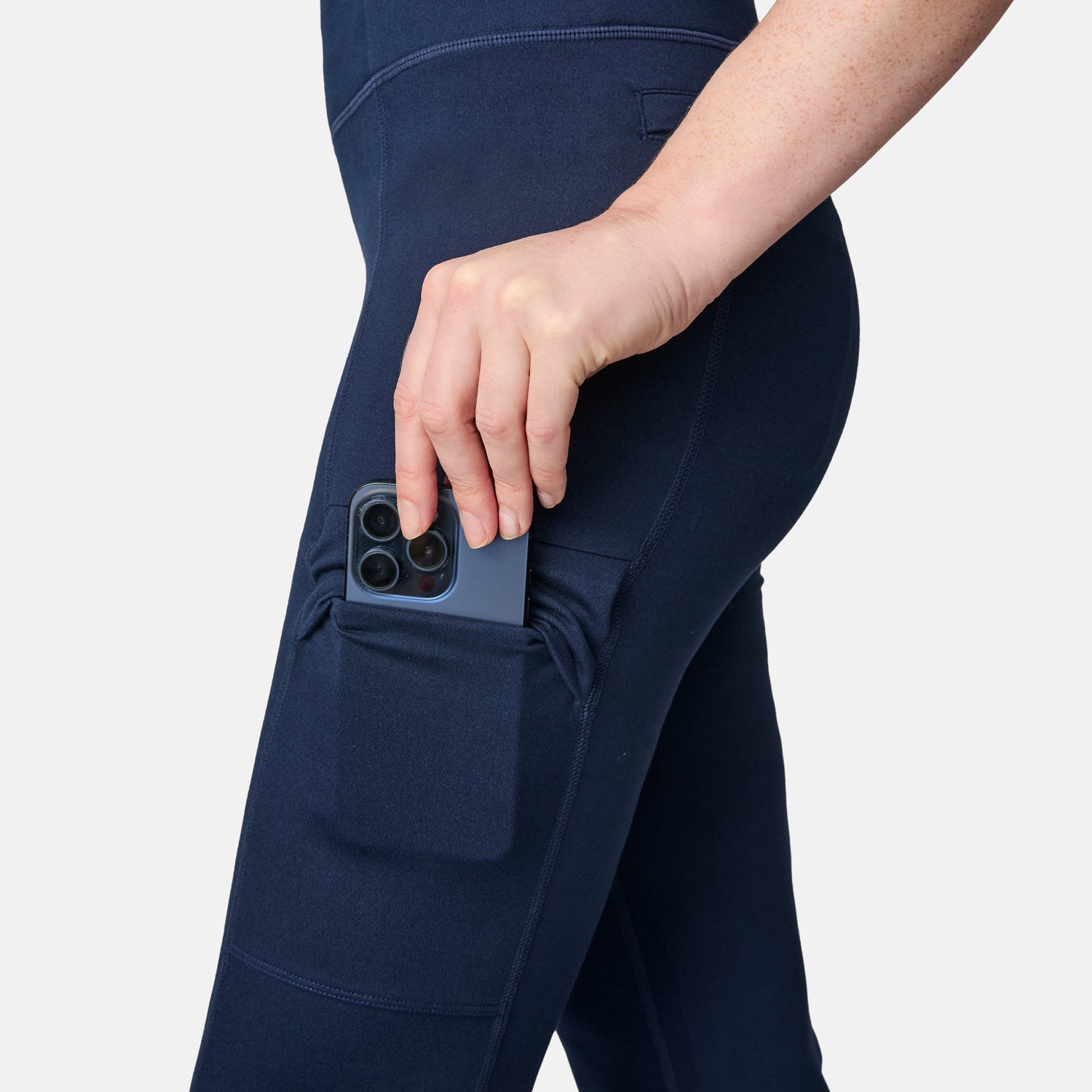 A woman in Free Country Women’s Trail 2 Town Flare Pants (UPF 50+) slips her smartphone into a thigh side pocket, fusing sun safety with handy storage.