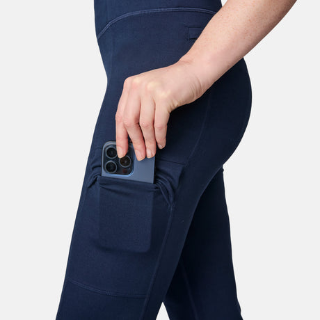 A woman in Free Country Women’s Trail 2 Town Flare Pants (UPF 50+) slips her smartphone into a thigh side pocket, fusing sun safety with handy storage.