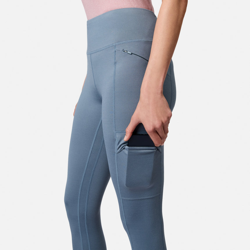 Free Country Women’s Trail 2 Town Legging in blue, featuring a high-waisted design, four-way stretch, a zippered hip pocket, and a side thigh pocket holding a smartphone.