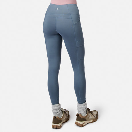 Free Country Women’s Trail 2 Town Legging in blue, featuring a high-waisted, four-way stretch design with side pockets, paired with grey socks and brown hiking shoes.